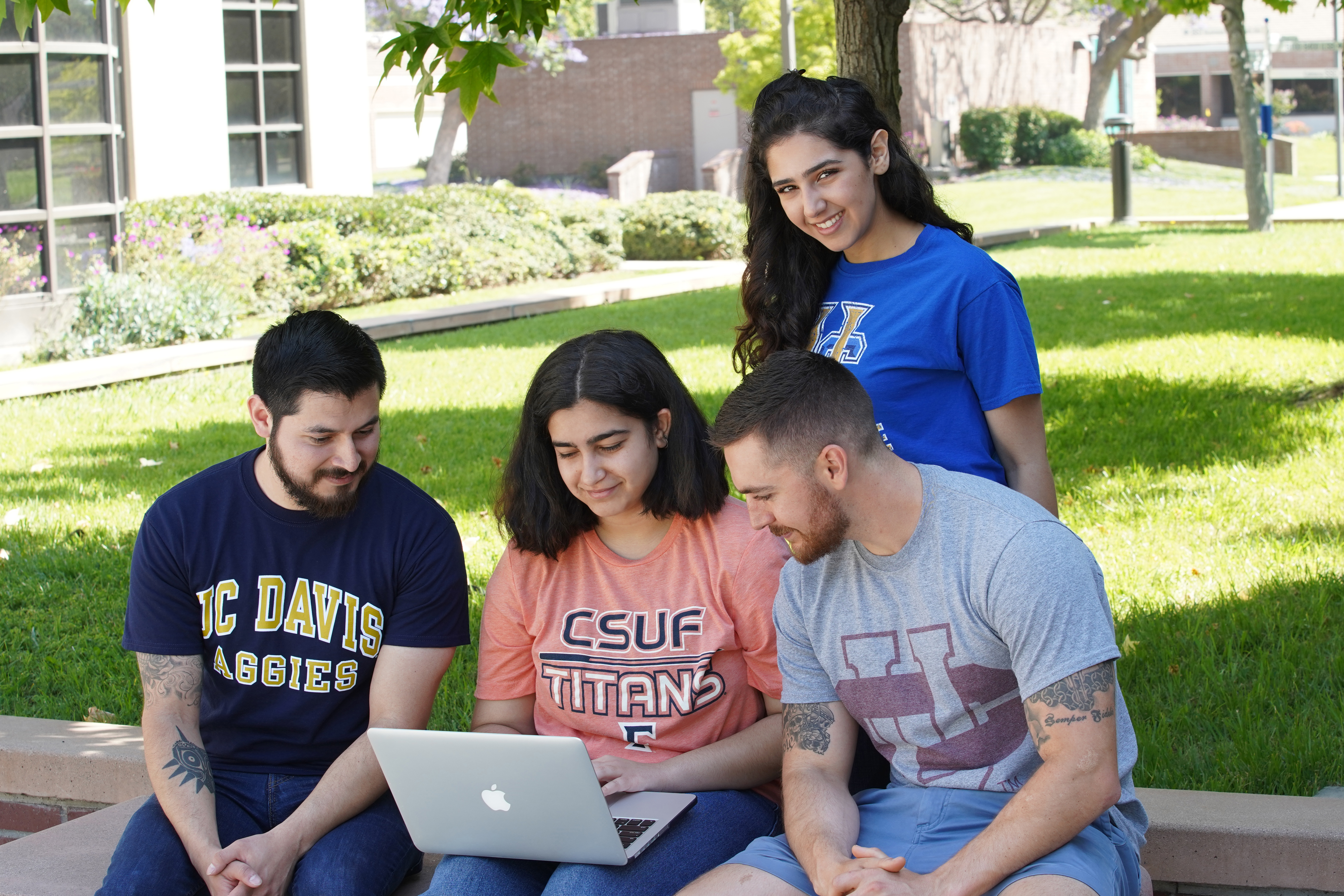 Photo of students wearing four-year college clothing and looking at a laptop